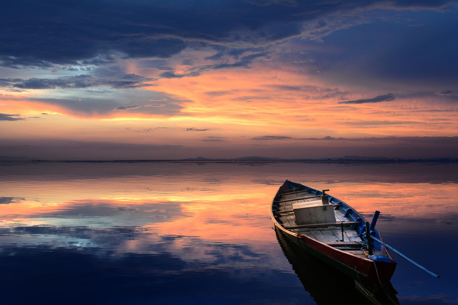 A wooden rowboat floats on calm water at sunset, colorful clouds and sky reflected in the still surface, embracing life changes in a tranquil moment.